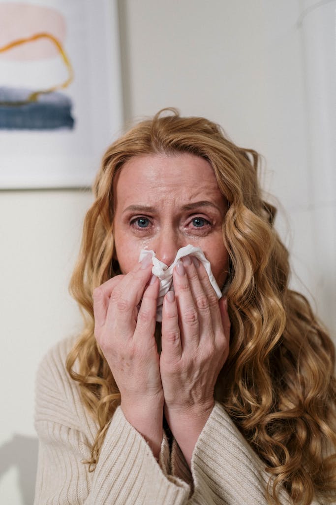 Woman appearing sick with tissue to her nose and watery eyes