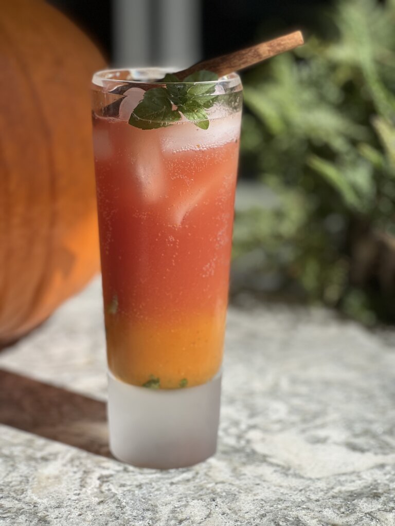 red and orange iced drink in a tall glass with sprig of mint