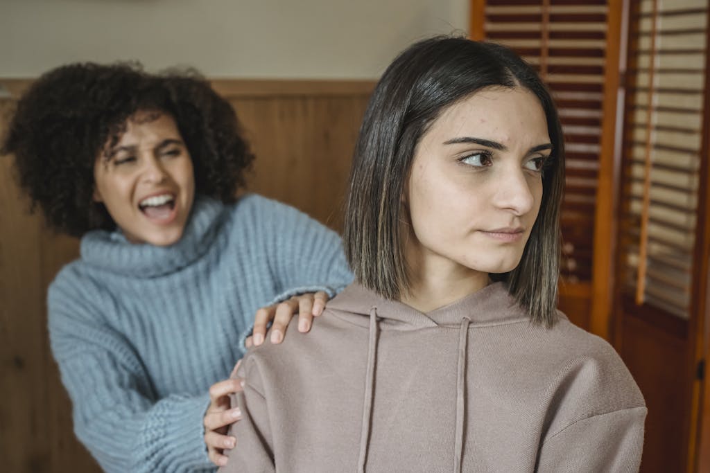 Upset female grabbing shoulder of other female who is ignoring during conflict
