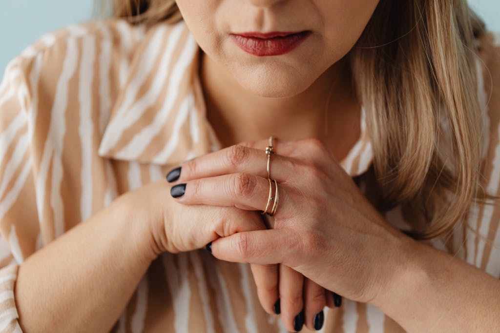 Close-up of a woman with clasped hands wearing rings, showing thoughtful expression.